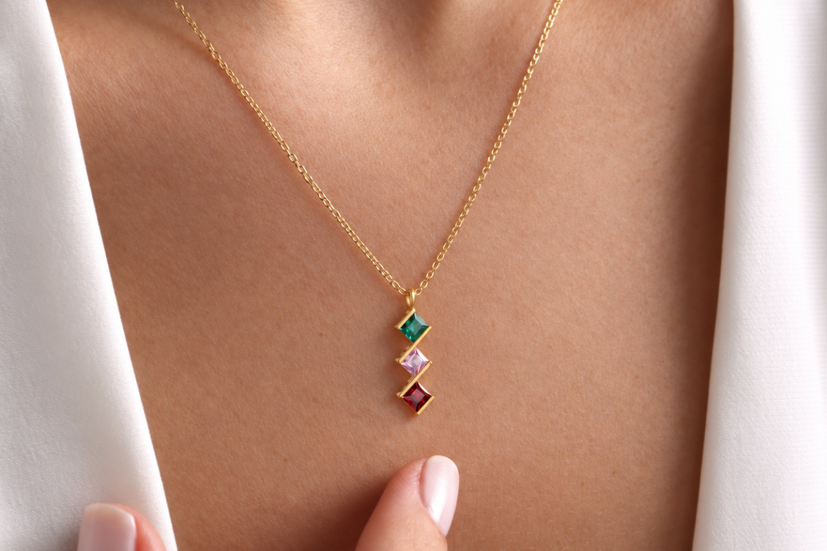 Family birthstone necklace with three square-set coloured stones on a gold-coloured chain, worn with a white shirt.